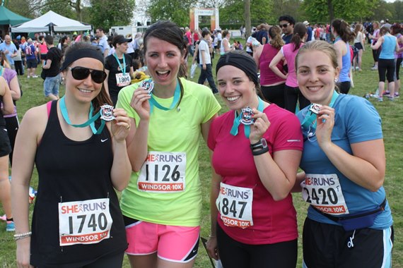 4 women in running outfits smile at the camera holding up their race medals