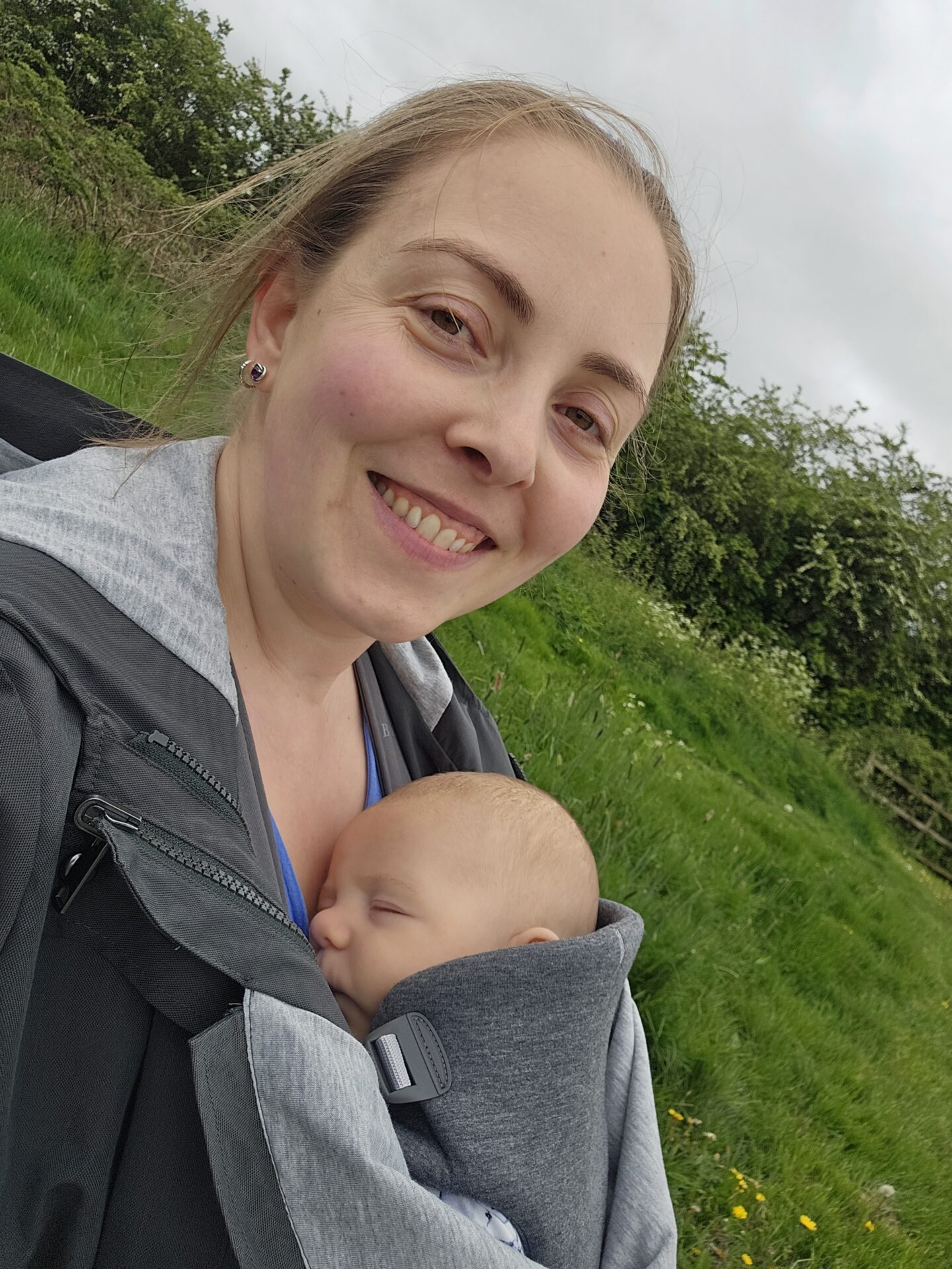 smiling woman is carrying a sleeping baby in a carrier on her front 