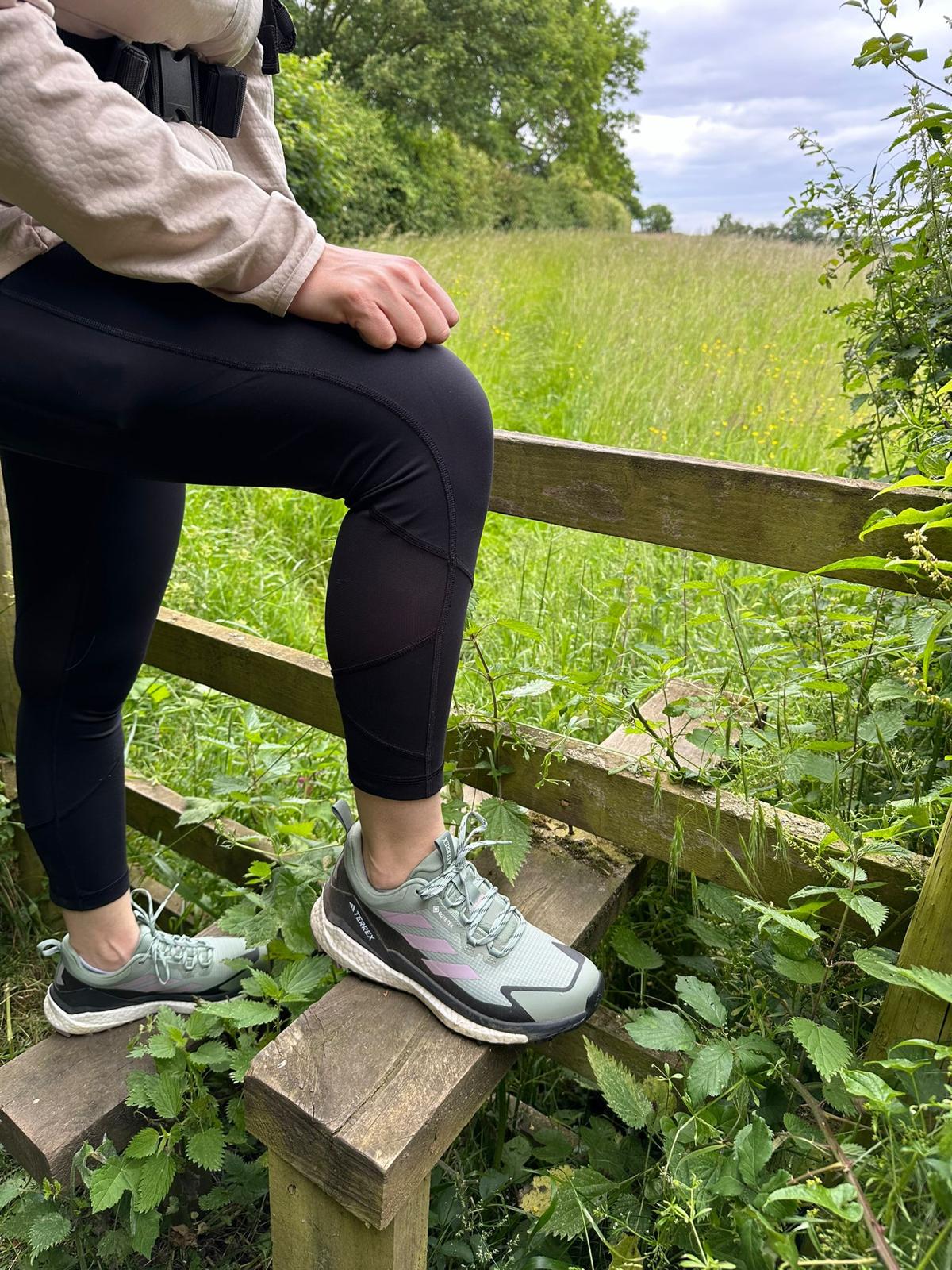 close up of woman's legs wearing adidas terrex hiking shoes, standing on a wooden stile. 