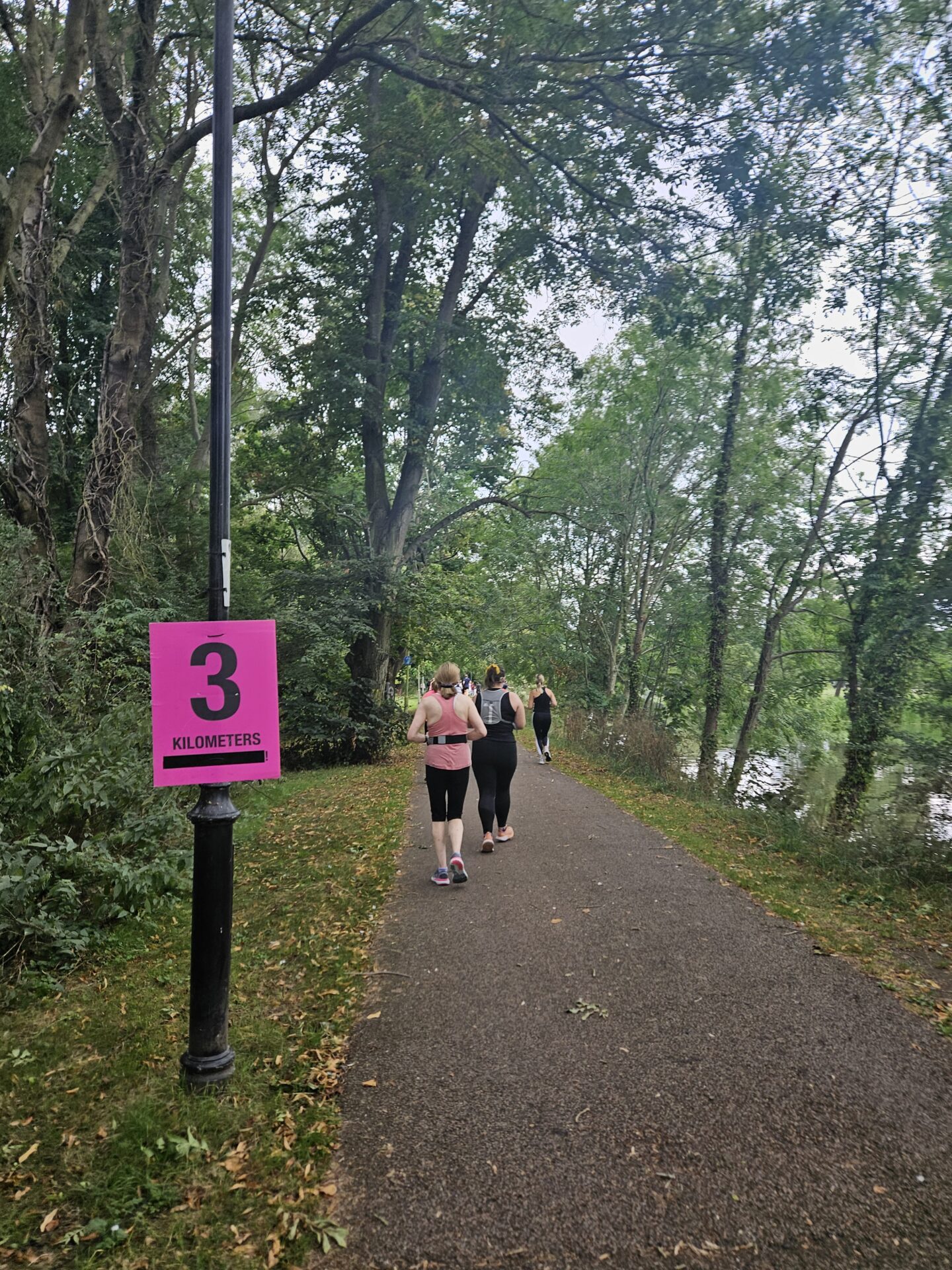 Pink sign says 3 kilometres with a path behind, surrounded by trees