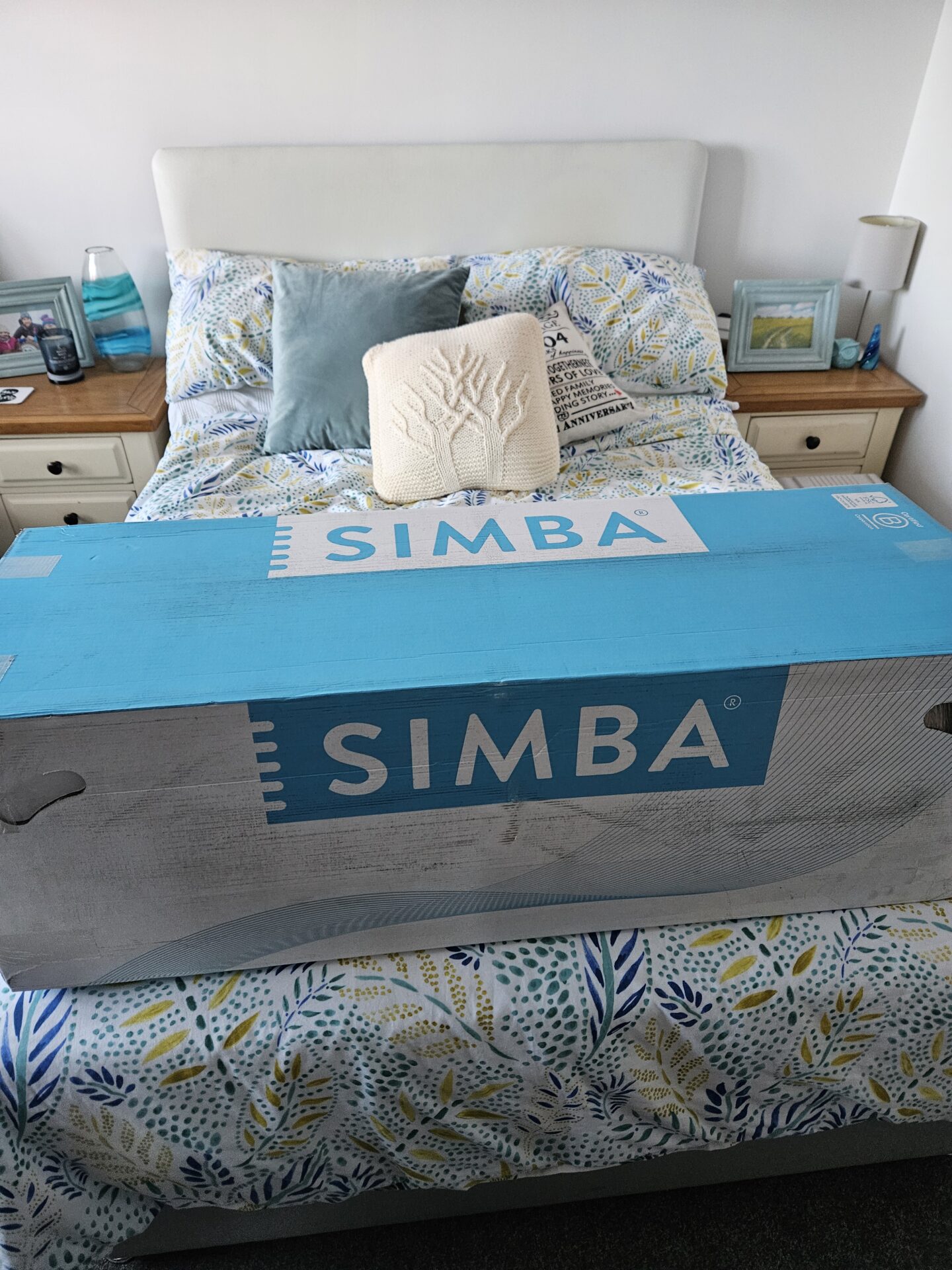 Blue and white Simba cardboard box sitting on the end of a double bed with blue and yellow flowery bedding 