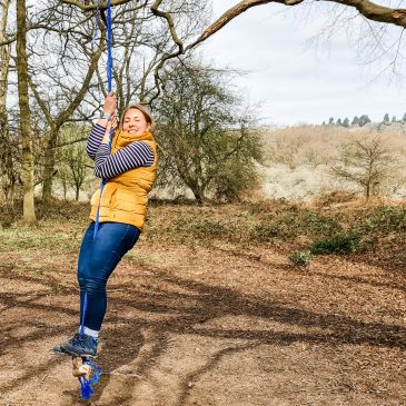 woman in yellow gilet swings on a rope swing smiling in the sunshin