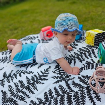 Baby in an adidas outfit is lying on a black and white playmat with toys around him