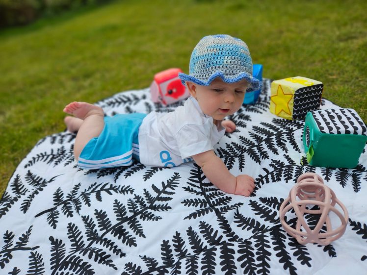 Baby in an adidas outfit is lying on a black and white playmat with toys around him