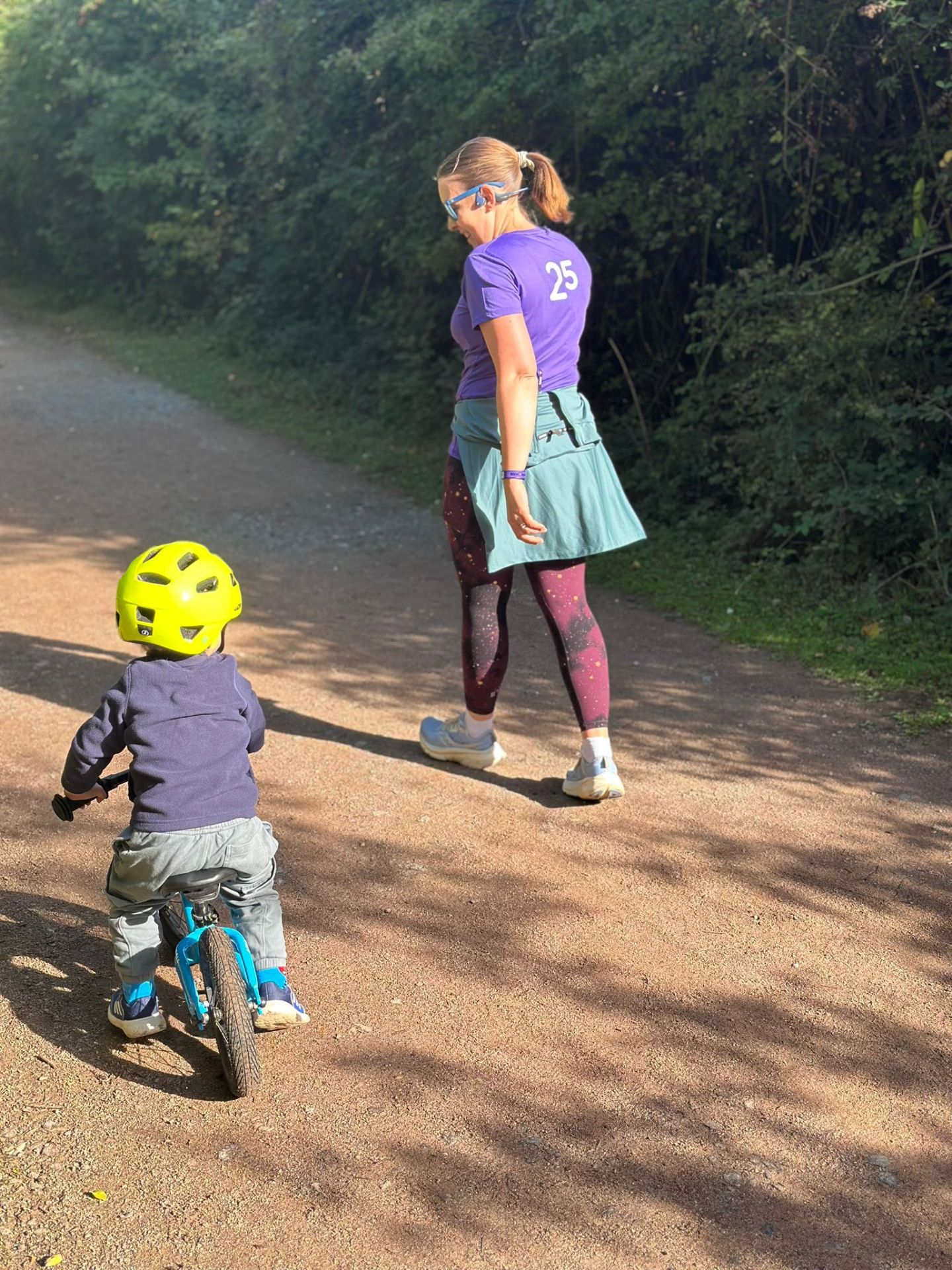 Toddler riding balance bike next to woman running at parkrun 