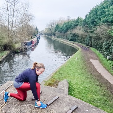 Woman wearing red leggings and black top kneels to tie her shoelaces on canal towpath